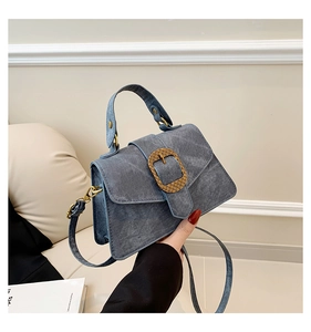 Close-up of blue denim bag featuring a large woven golden buckle and leather top handle