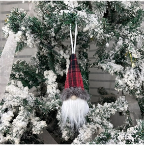 Red and black plaid Christmas gnome ornament hanging on a snowy tree branch