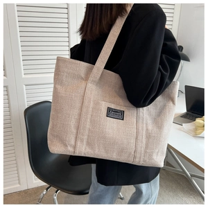Minimalist oatmeal canvas tote bag shown with a wide shoulder strap on a female model