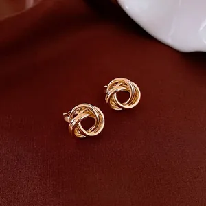 Minimalist intertwined triple gold hoop earrings on elegant silk fabric background