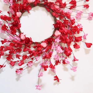 Close-up of heart wreath with red paper flowers and pink ornaments on vine base