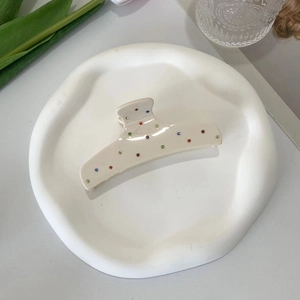 Detail view of a beige acetate hair claw clip with colorful polka dots on a white plate