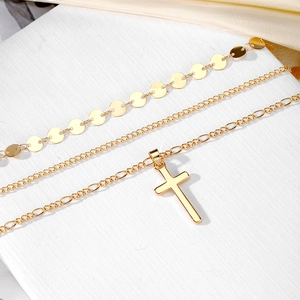 Detailed view of layered gold cross necklaces with Figaro chain and polished discs