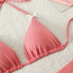 Detail of red vichy check bikini top with white bows on plush background