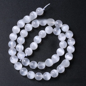 Detailed view of white selenite round beads with silk sheen and cat eye effect on black surface