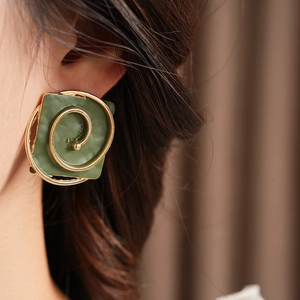 Close-up of vintage square spiral earrings in gold and green enamel on a model
