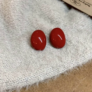 Close-up of elegant red enamel oval hoop earrings on soft grey knit fabric