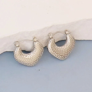 Detail of silver irregular geometric earrings with textured dot pattern on stone pedestal