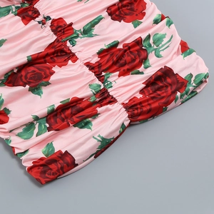 Detail of pink satin dress featuring red rose prints and elegant ruched texture design