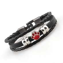 Detail of multi-layer black leather bracelet featuring a vibrant red paw print charm