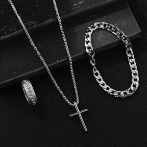Detailed view of silver cross pendant necklace, cuban chain bracelet, and textured ring set