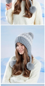 Detail of Fair Isle knit earflap hat with grey faux fur pom-poms and geometric pattern