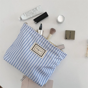 Flat lay of blue striped makeup bag with zipper showing brushes and cosmetics inside