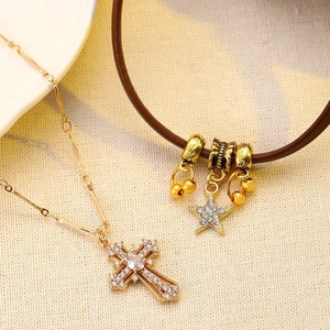 Detailed shot of golden cross necklace and brown leather bracelet on textured fabric
