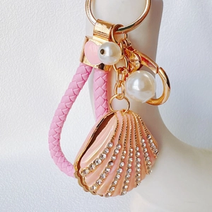 Macro view of pink enamel shell keychain with rhinestones, pearls, and woven leather cord