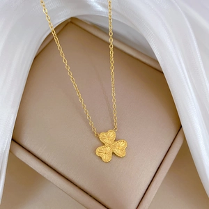Macro shot of gold clover pendant necklace with fine texture on beige jewelry box