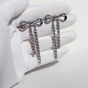 Elegant silver bow earrings with sparkling rhinestone tassels held on white background