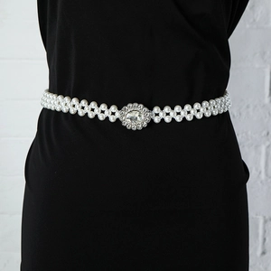 Detailed view of elastic pearl waist belt with floral rhinestone buckle on black dress
