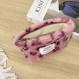 Pink leopard plush cosmetic pouch with zipper on a wooden table with lifestyle props