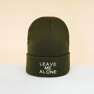 Detailed close-up of Leave Me Alone white embroidery on a dark green knitted beanie hat