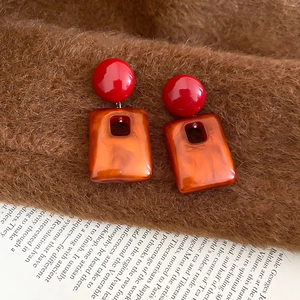 Detail of retro acrylic rectangular drop earrings with orange marble texture on brown fabric