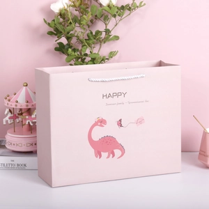 Rosa Geschenkbeutel mit Dinosaurier-Muster und weißem Tragegriff auf Dekotisch