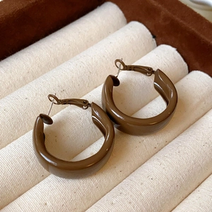 Gros plan de créoles en résine marron en forme de C avec tiges en métal sur coffret