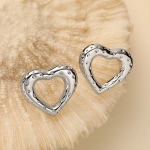 Macro view of silver heart stud earrings with dot texture on beige coral background