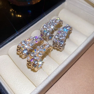 Close-up of gold C-shaped earrings with inlaid white pearls and sparkling rhinestones