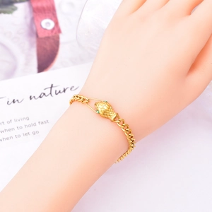 Snake head bracelet with green stones and gold Cuban chain on a woman's wrist