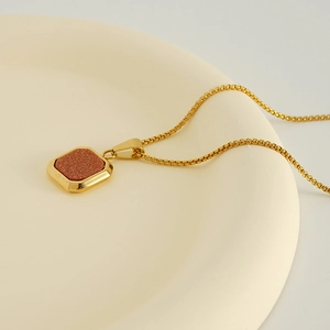 Macro d'un pendentif carré doré avec grès brun sur une assiette en céramique blanche