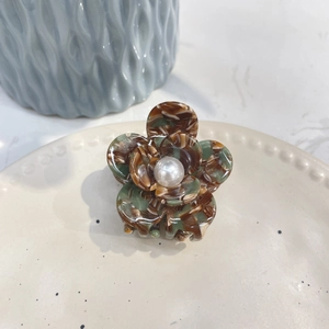 Detail of acetate flower hair claw with amber petals, pearl center on ceramic plate