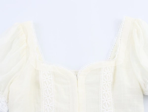 Close-up of square neckline with lace trim and puff sleeves on cream crop top shirt
