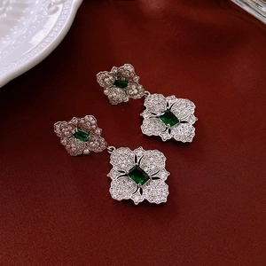 Close-up of silver floral earrings with emerald stones on a luxury red satin backdrop