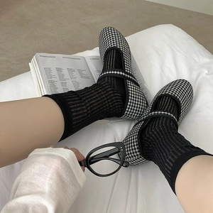 Close-up of gingham Mary Jane shoes with black striped socks on a white bed