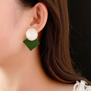 Close-up of model wearing white round and dark green diamond-shaped resin earrings