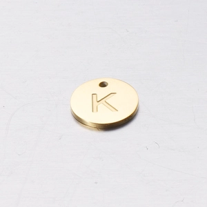 Macro shot of 12mm gold stainless steel round charm featuring engraved letter K detail