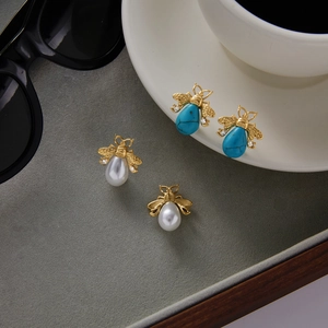 Detail view of bee-shaped gold earrings with pearls, turquoise stones, and small crystals
