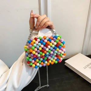 Detail of a colorful beaded mini bag with silver chain strap held by a manicured hand