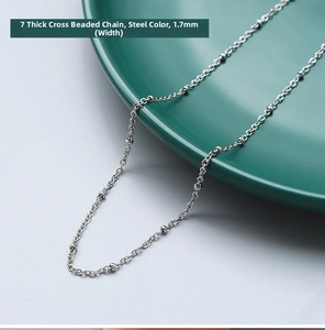 Detail of 1.7mm silver steel cross chain with small beads on dark green ceramic plate