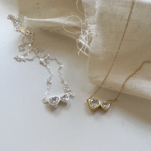 Close-up of gold and silver heart-shaped zircon necklaces on a soft beige fabric background