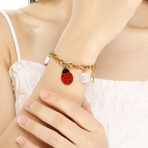 Detail of a gold chain bracelet featuring a red enamel ladybug and a white pearl bead