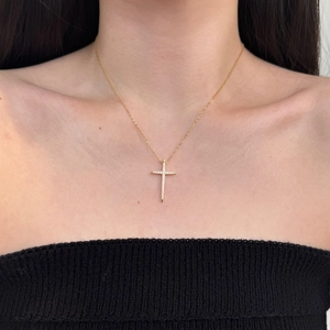Close-up of a gold cross pendant necklace with white stones worn by a model