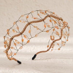 Detail of handcrafted bridal headband with gold wire and peach beads on light surface