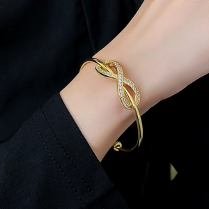 Macro shot of gold-plated infinity bracelet featuring cubic zirconia stones on a model wrist