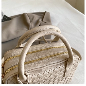 Detailed top view of beige woven leather handbag with double gold zippers and handles