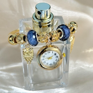 Detail of gold beaded bracelet watch with blue charms and owl pendant on silk cloth