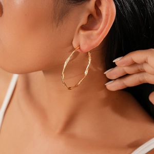 Close-up of golden twisted geometric hoop earrings worn by a model in a high-fashion style