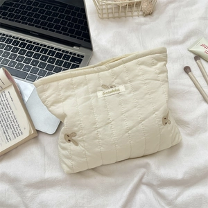 Detailed view of cream quilted makeup bag with bunny embroidery and brand logo