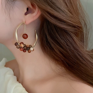 Close-up of model wearing C-shaped gold hoops with woven sandalwood beads and hanging pearls